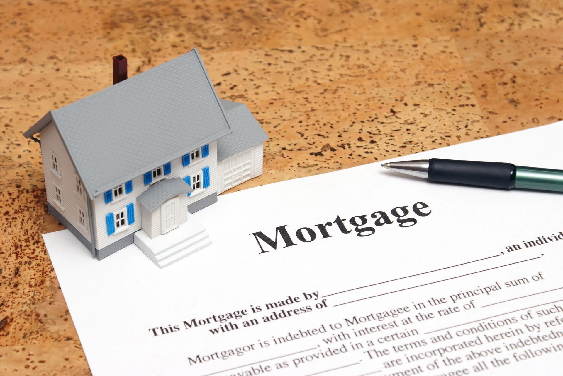 Model house next to a mortgage document and pen on a wooden surface.