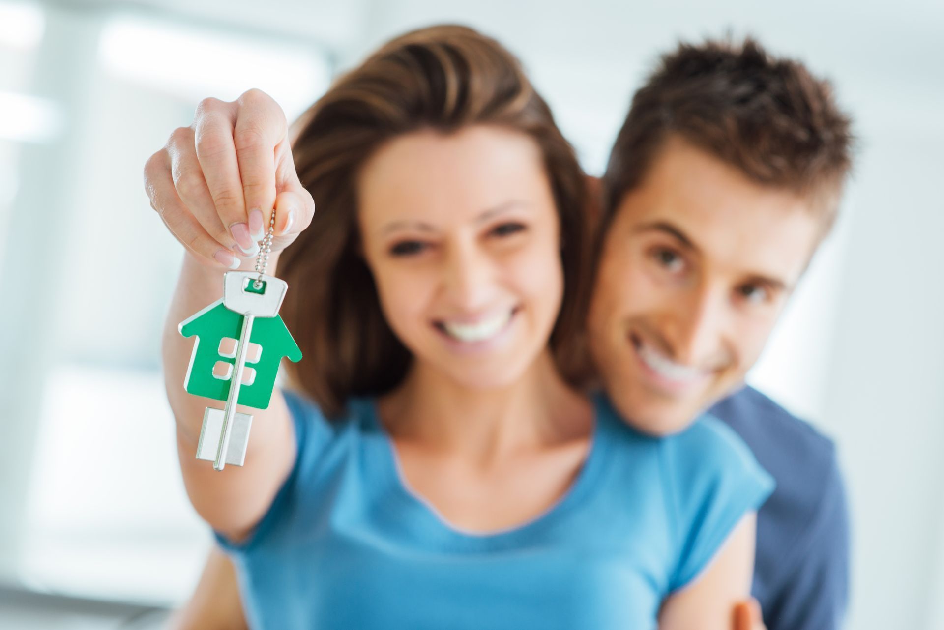 Smiling couple holding house keys with green house-shaped keychain.