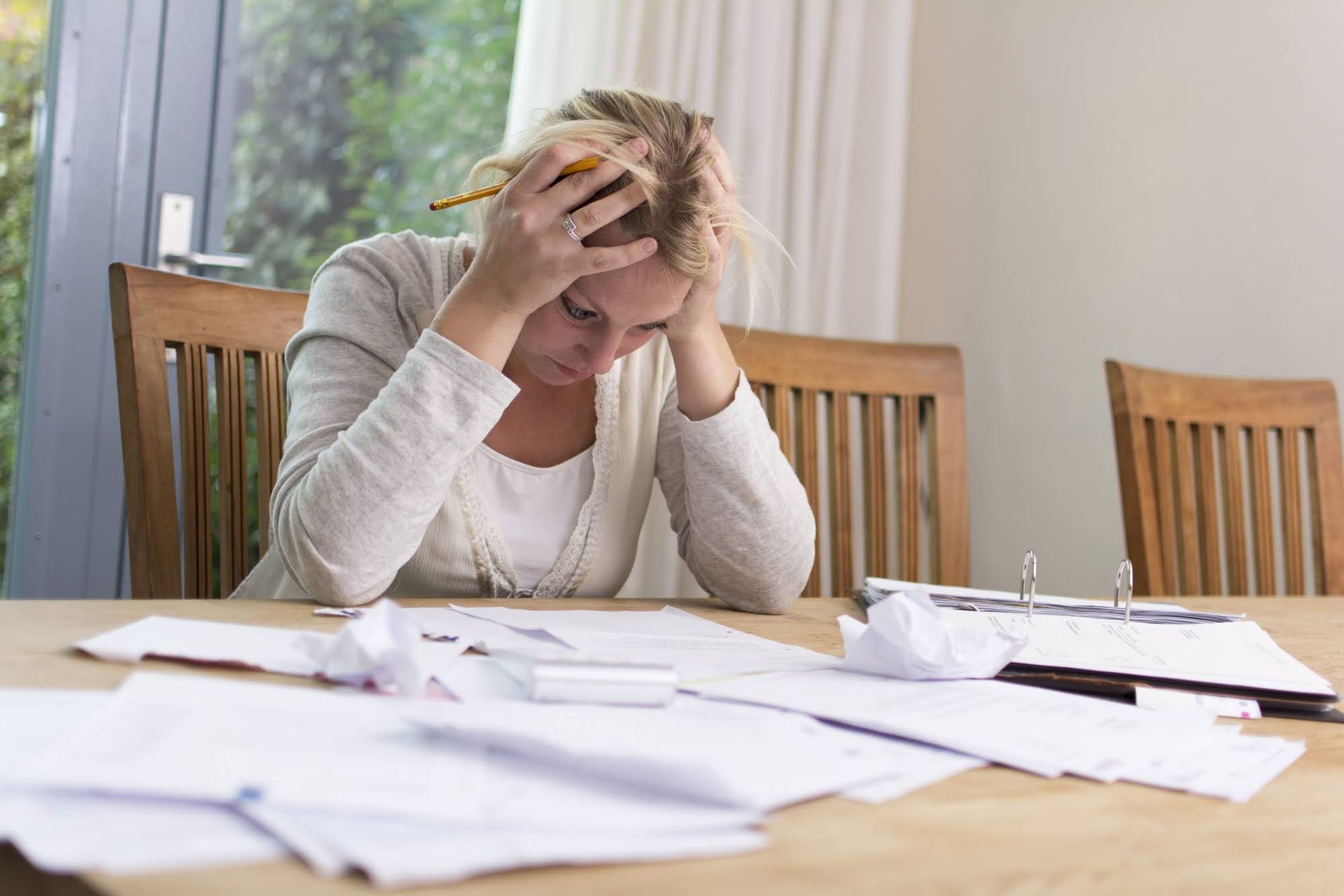 Woman with head in hands, stressed at a table with papers, calculator, and crumpled notes.