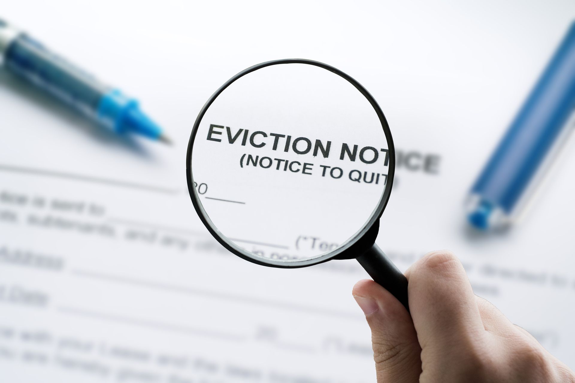 Magnifying glass over an eviction notice. A hand holds the magnifying glass, two pens are on the paper.