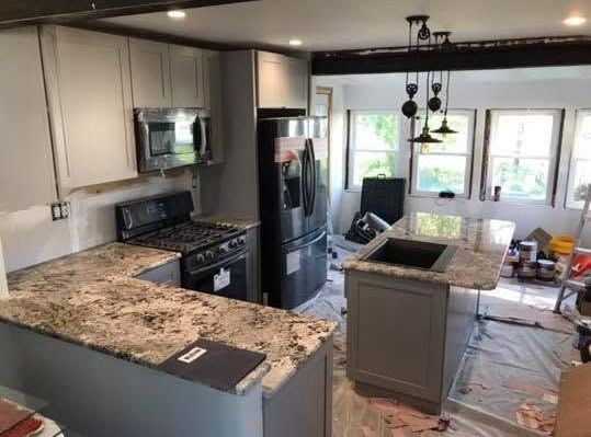 Modern kitchen with granite counters, black appliances, island, and bright windows overlooking a patio