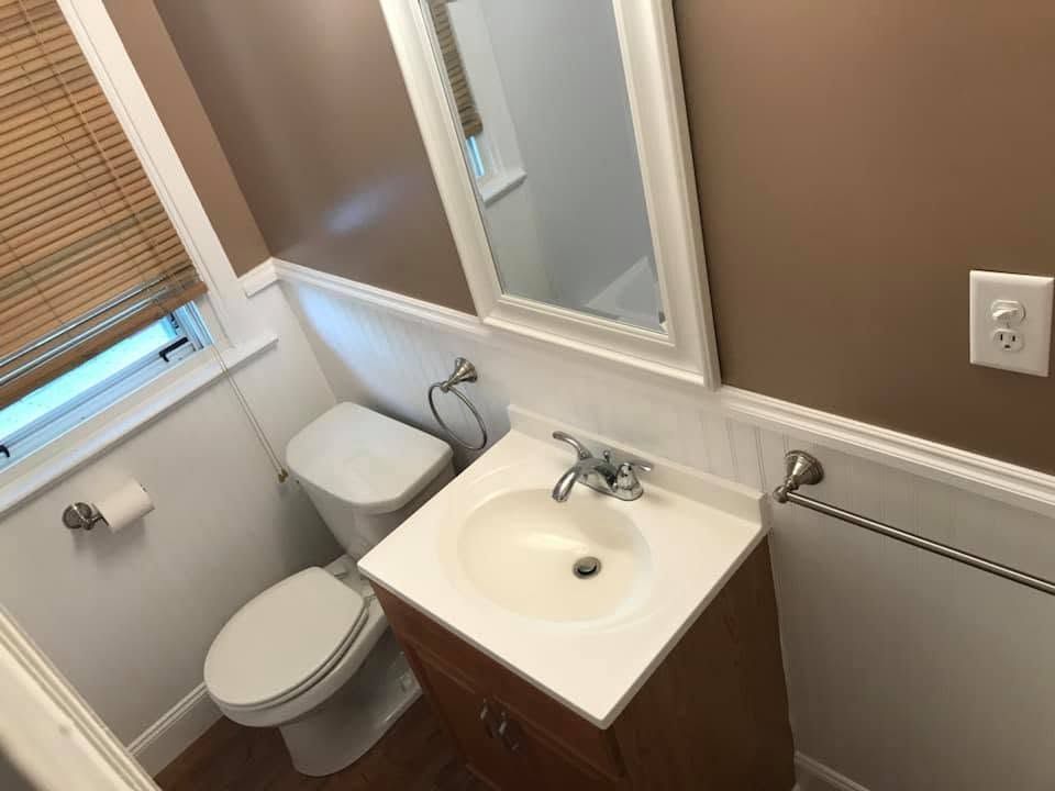 Small bathroom with toilet, sink, mirror, window blinds, and towel bar.