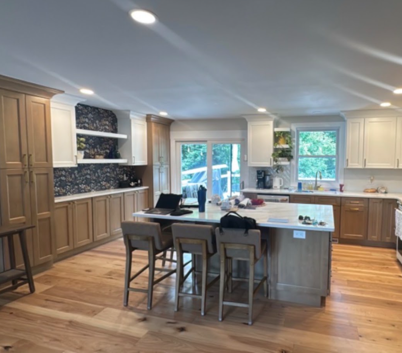 Spacious modern kitchen with island, wood floors, white cabinets, and a dining table near bright windows