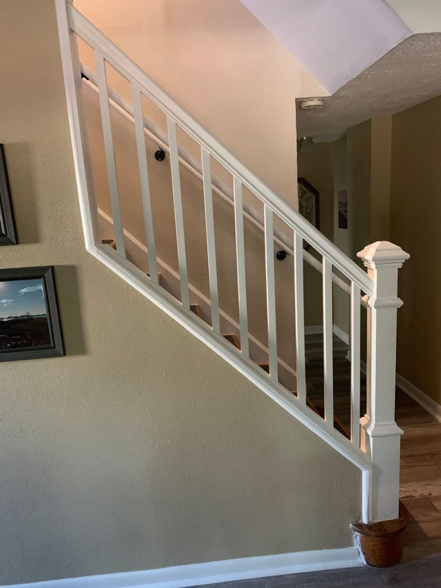 Interior staircase with white railing and beige walls, leading up to a landing.