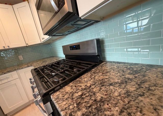 Modern kitchen with stainless steel stove, granite countertop, and light blue tile backsplash