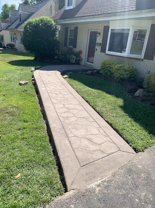Concrete walkway leading to a house entrance across a green front lawn
