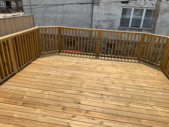 Wooden rooftop deck with curved railing and concrete building walls in the background