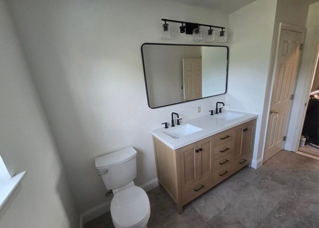 Bathroom with white toilet, wood vanity, large mirror, and carpeted floor.