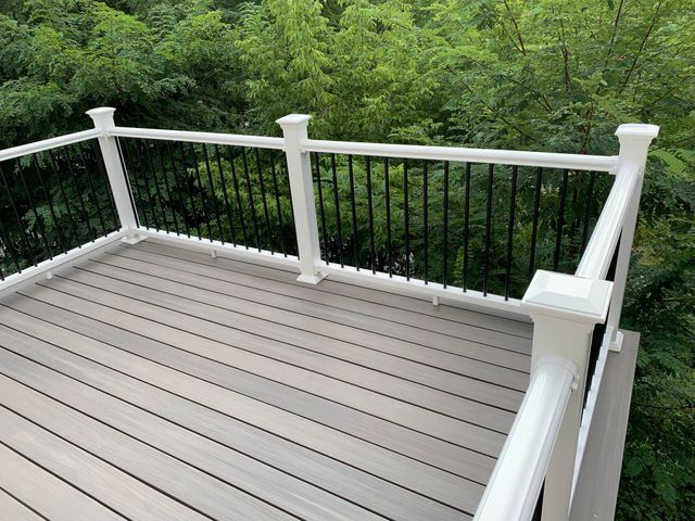 Wooden deck with white railing overlooking dense green trees.