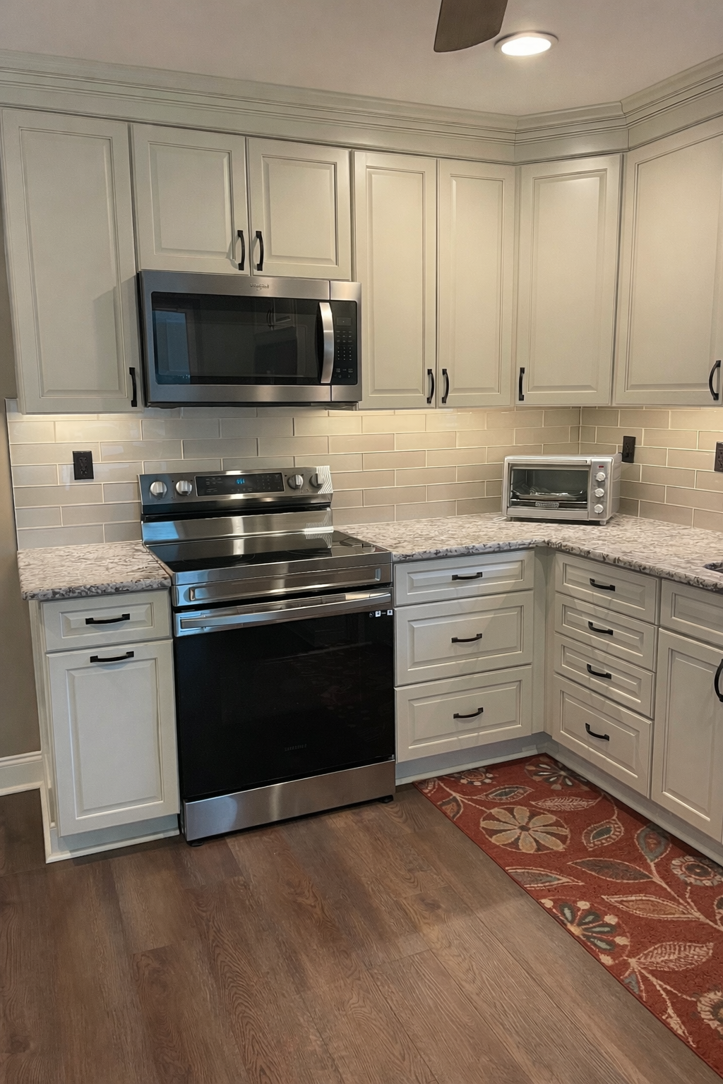 Modern kitchen with white cabinets, black stove and microwave, wood floor, and a red patterned rug.