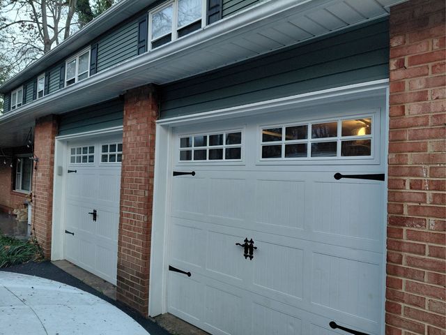 Two white garage doors on a brick townhouse, with a gray awning above and lit windows.