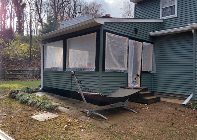 Small screened porch attached to a green house, with a damaged front panel and steps leading to the yard