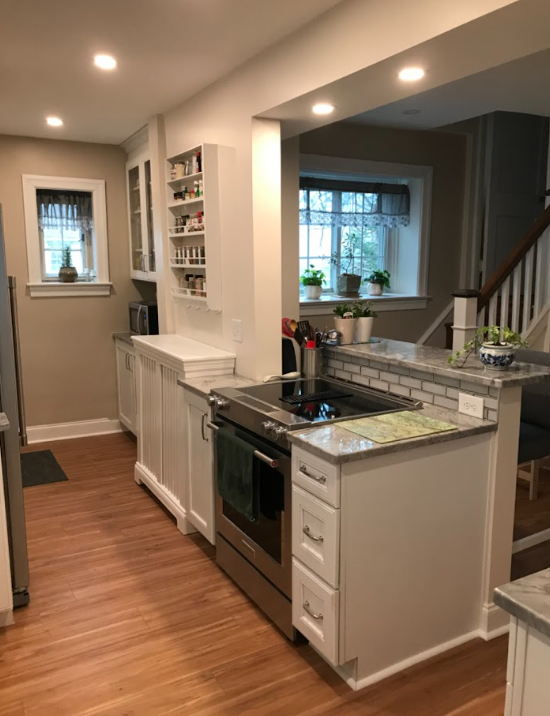 Narrow kitchen with white cabinets, stainless stove, granite counters, and a window by the staircase.