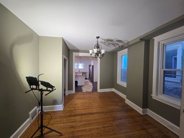 Empty living room with hardwood floors, gray walls, windows, and an exercise bike near the left wall.