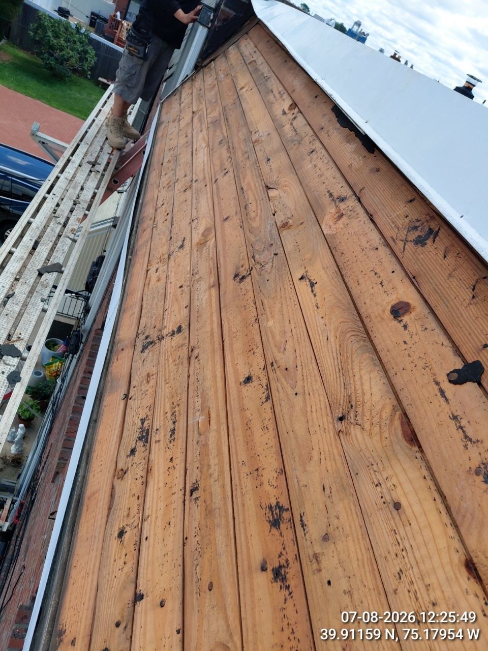 Close-up of a worn wooden roof deck beside a white metal roof edge and ladder.