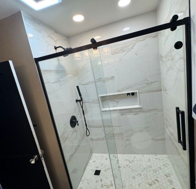 Modern walk-in shower with glass doors, marble tile walls, black fixtures, and a handheld showerhead