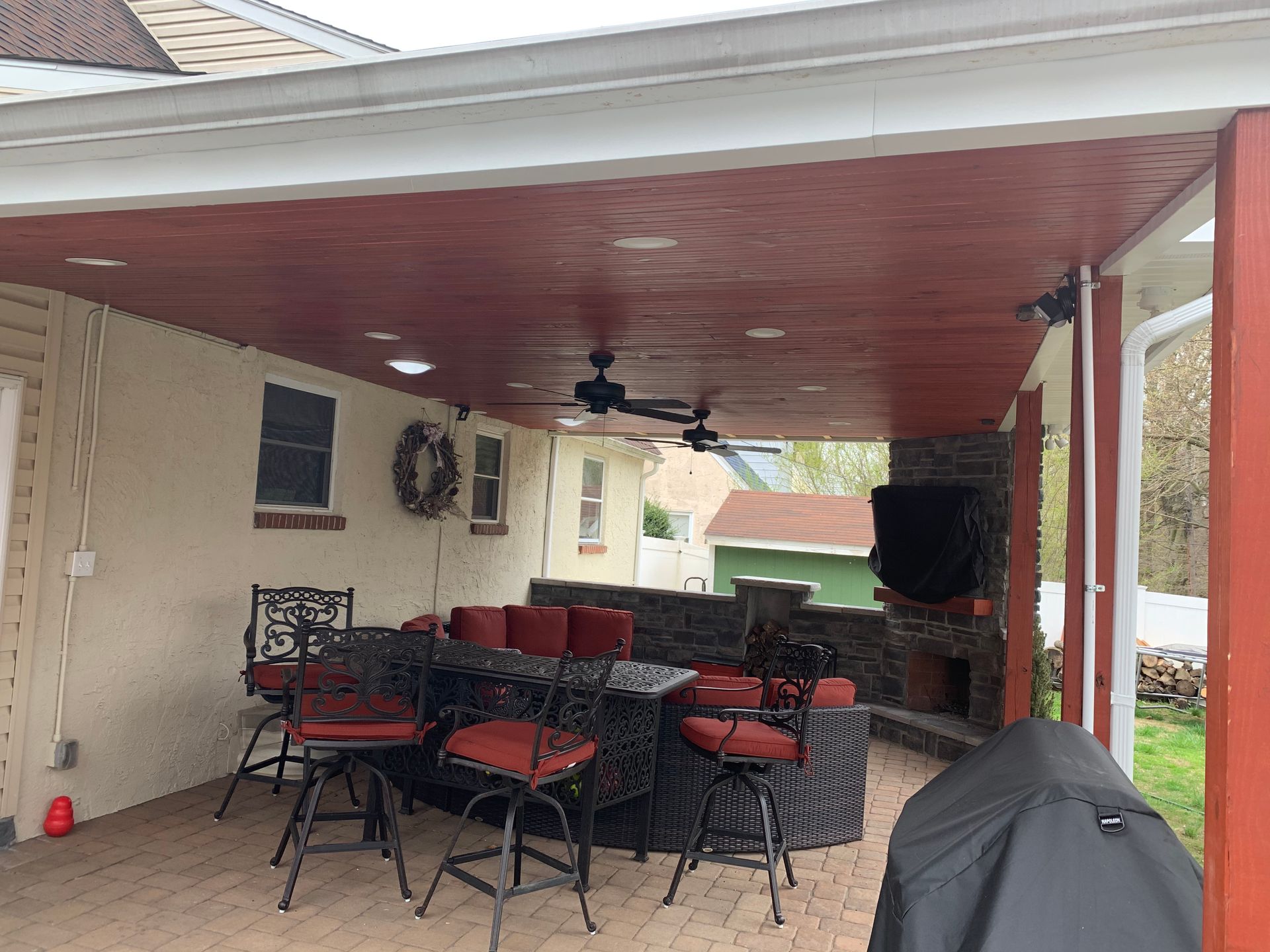 Covered patio with black and red outdoor seating, ceiling fan, and a grill in the background