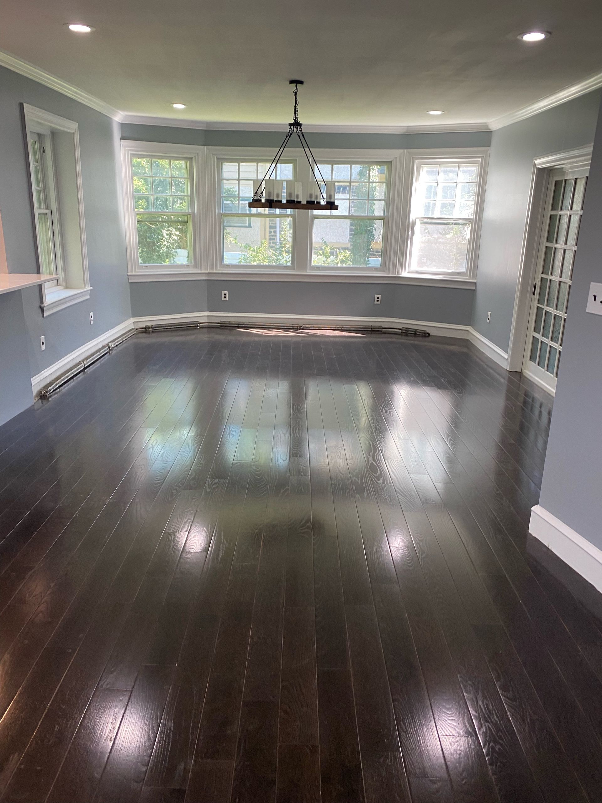 Empty dining room with dark hardwood floors, gray walls, windows, and a hanging light fixture