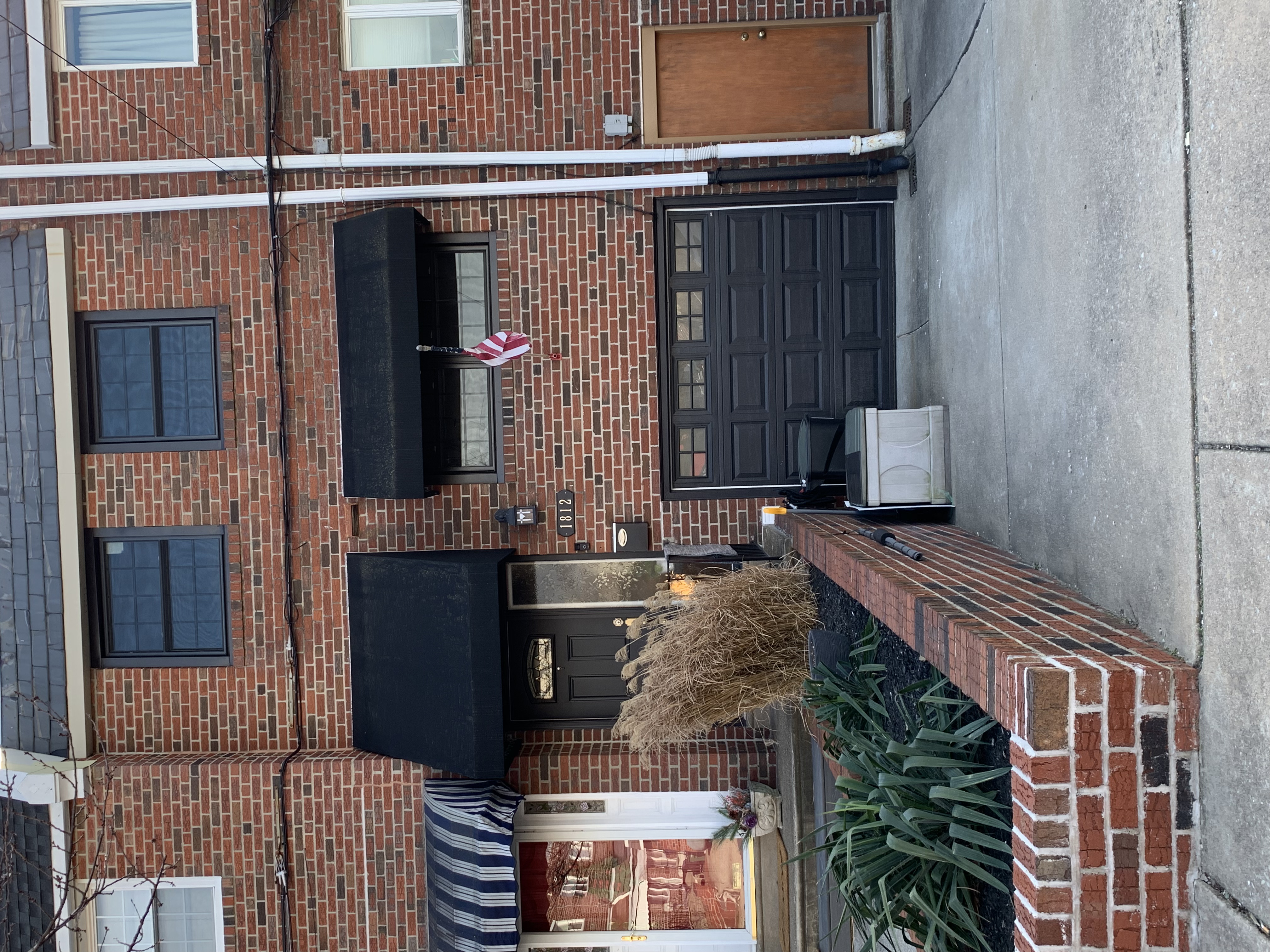 Brick row house with black awnings, garage, and a small front garden by the sidewalk