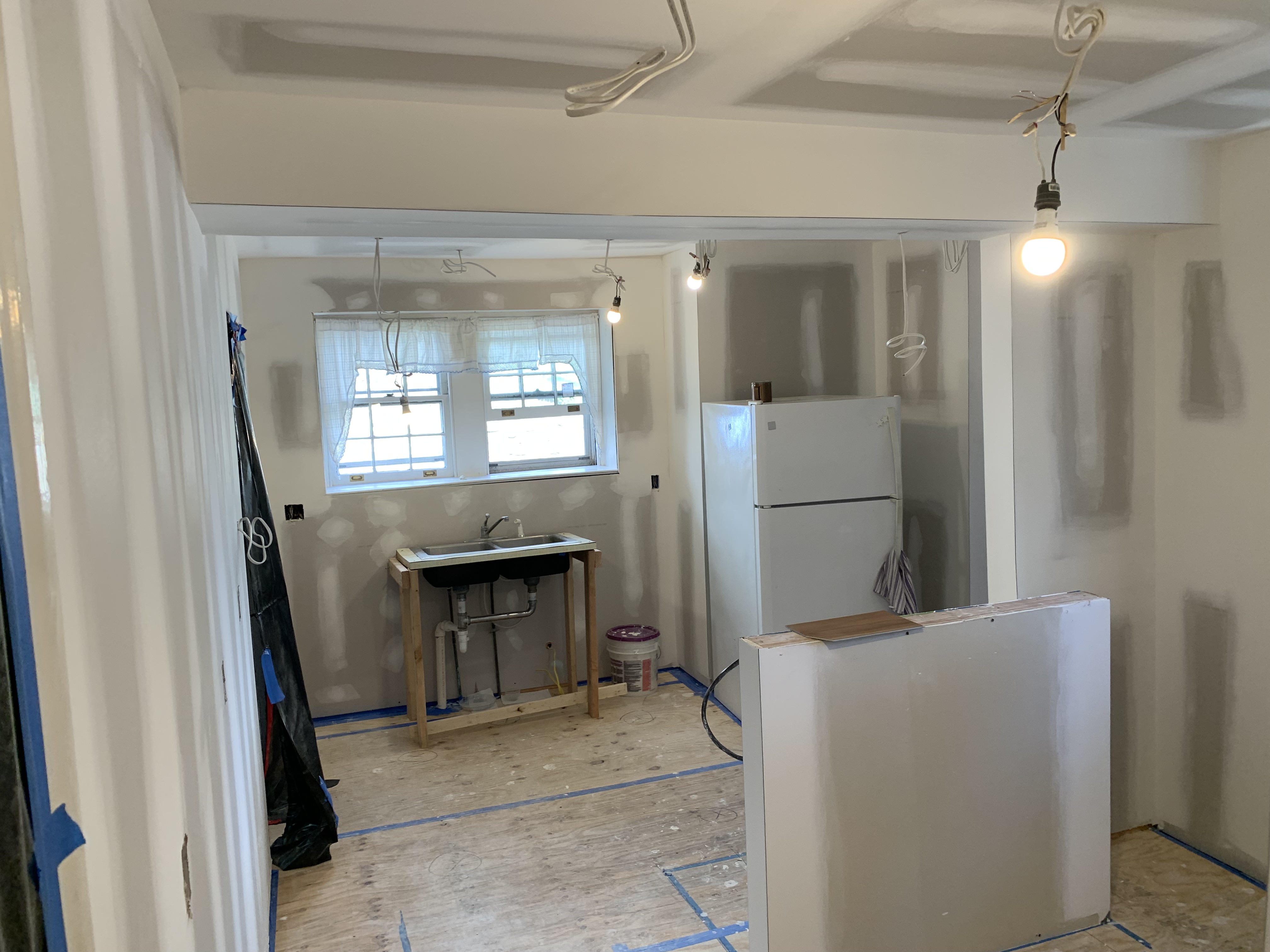 Renovated room with white walls, exposed ceiling lights, window, small table, and refrigerator