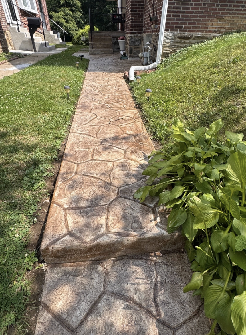 Brick walkway with cracked concrete steps beside a grassy slope and house exterior