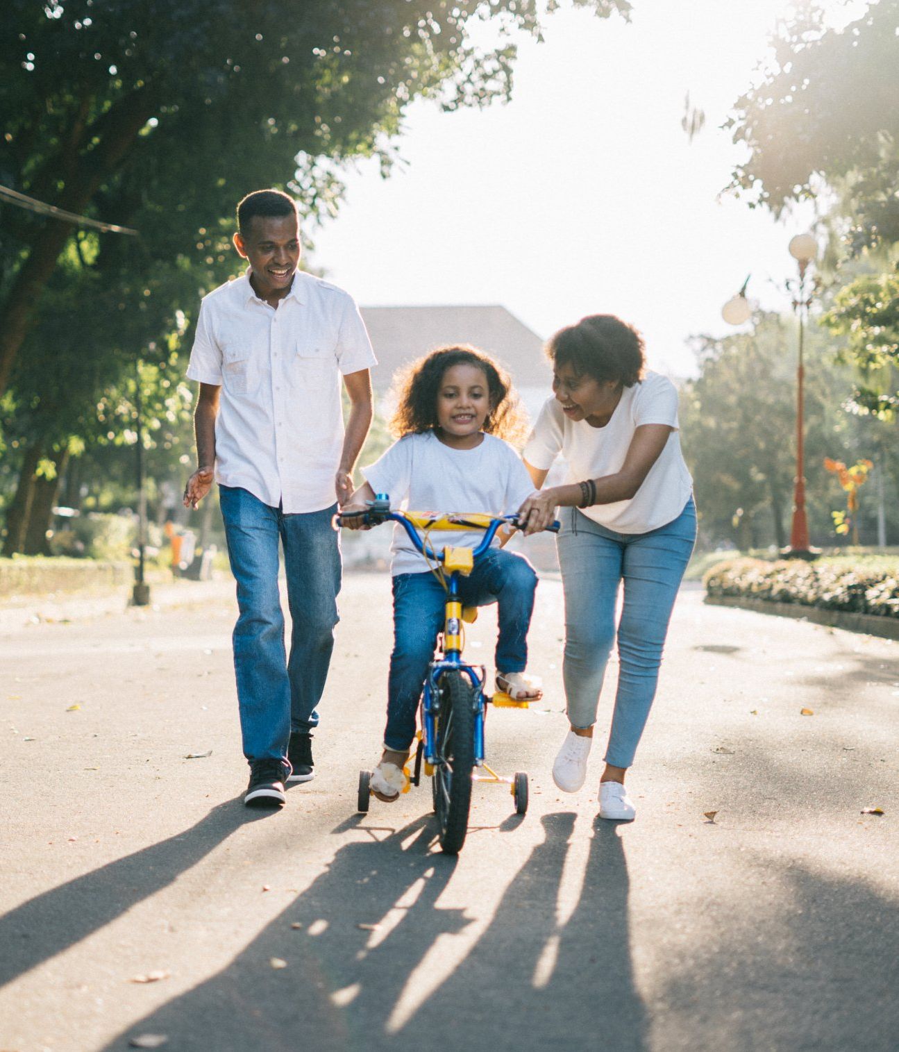 a little girl is riding a bike with her parents behind her