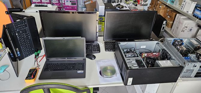 Banco da lavoro con diversi computer portatili, monitor e componenti per computer disposti in un negozio di elettronica.