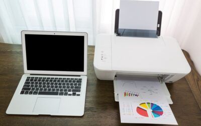 Un computer portatile accanto a una stampante bianca che stampa un grafico a torta a colori su una scrivania di legno.