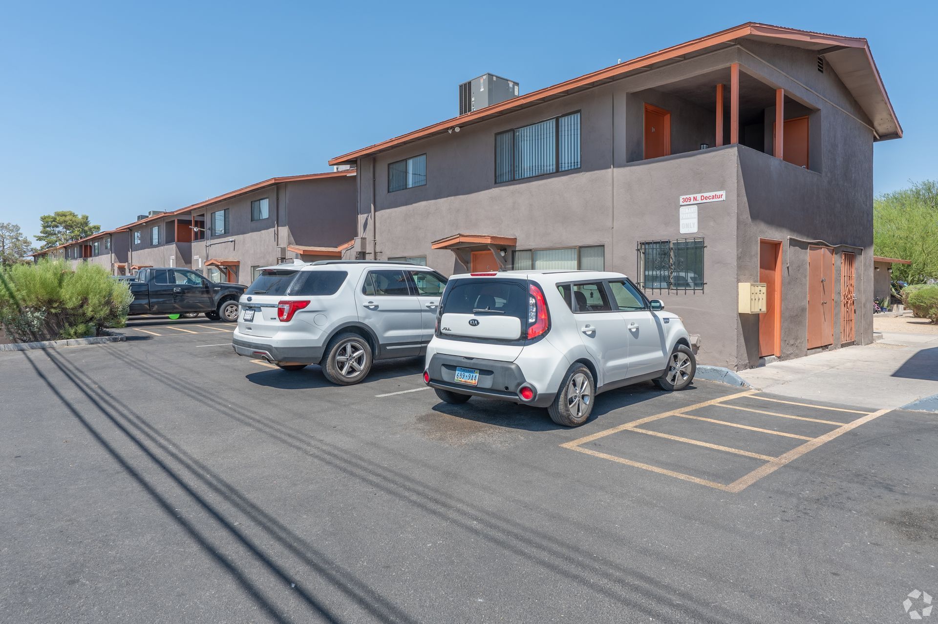 Two parked cars beside a brown apartment building on a sunny street.