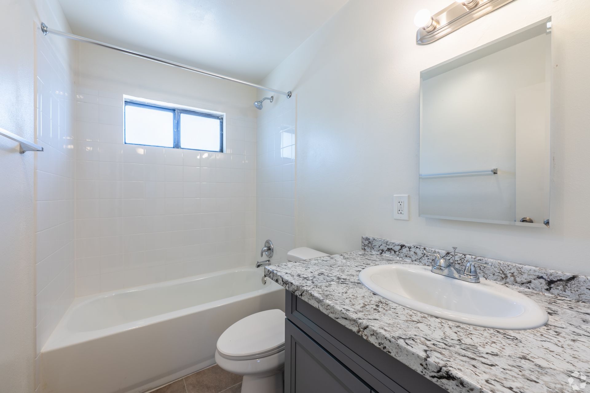 Bright bathroom with bathtub, granite vanity, mirror, and small window