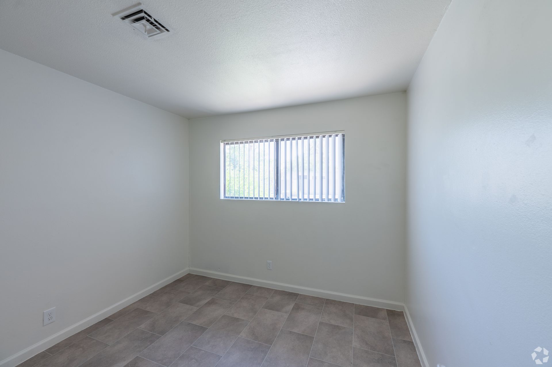 Empty gray bedroom with carpeted floor and a window with blinds