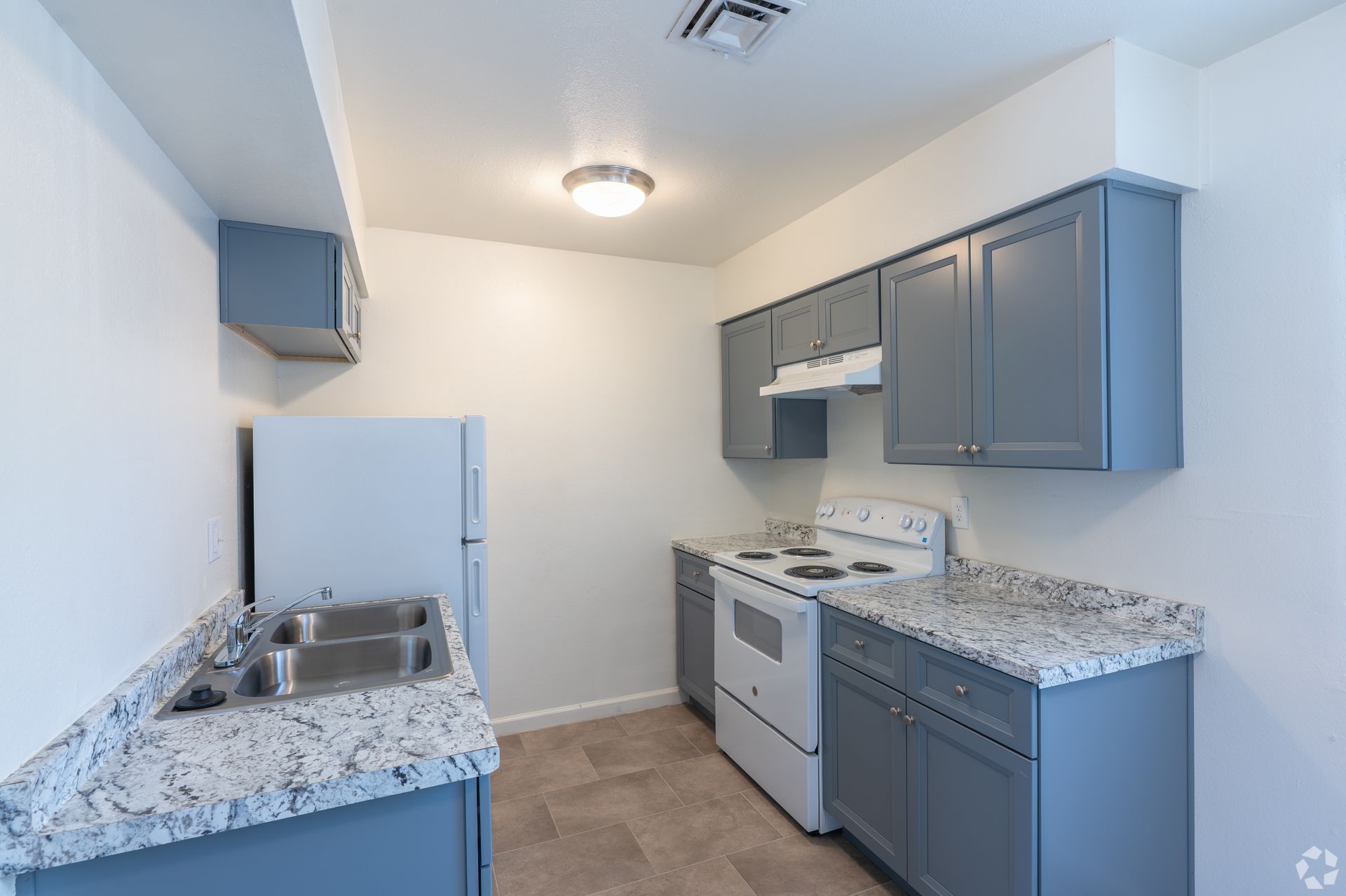 Small white kitchen with blue cabinets, white appliances, and speckled countertops.