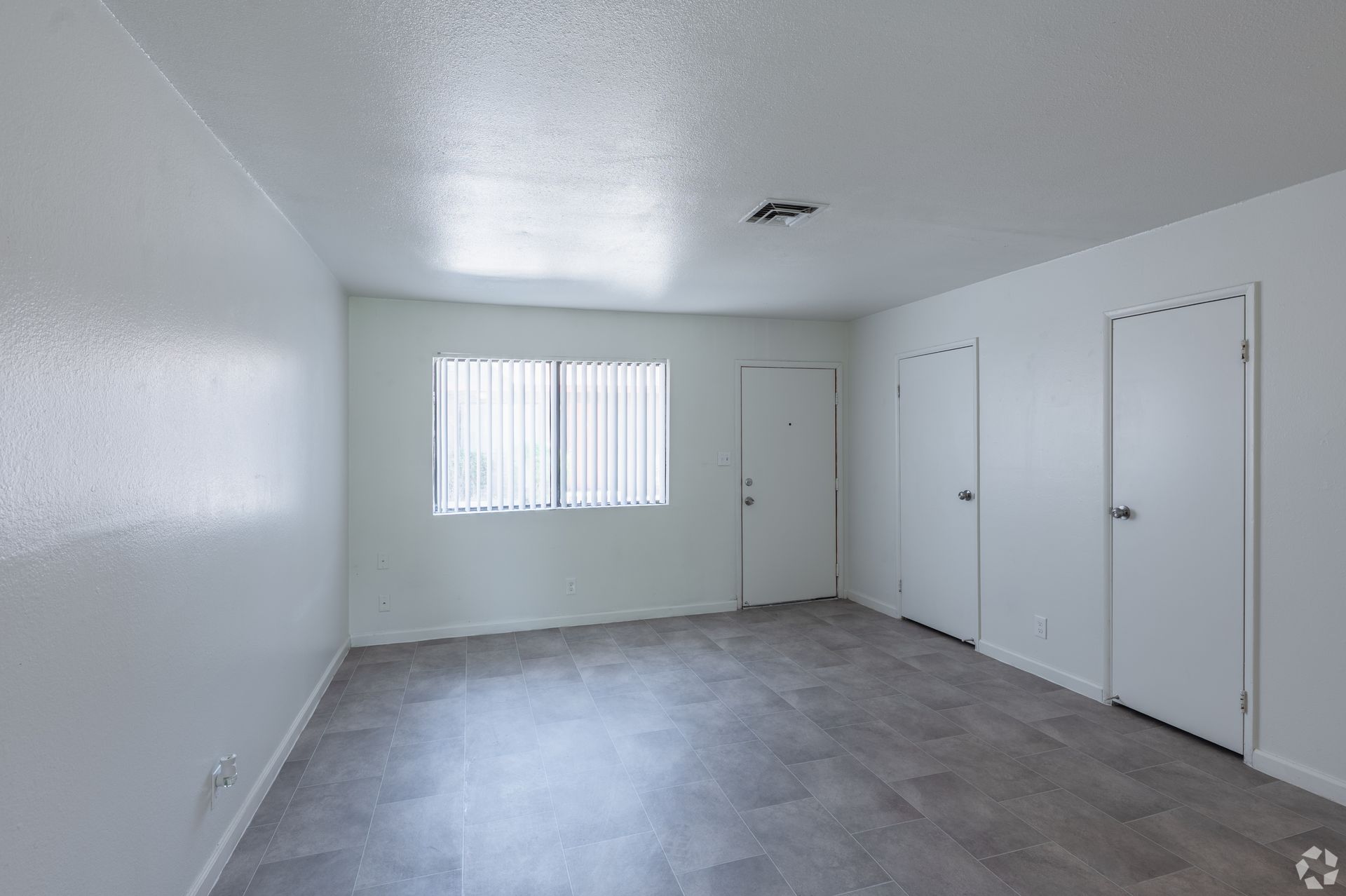 Empty white room with gray carpet, a window, and two closed doors.