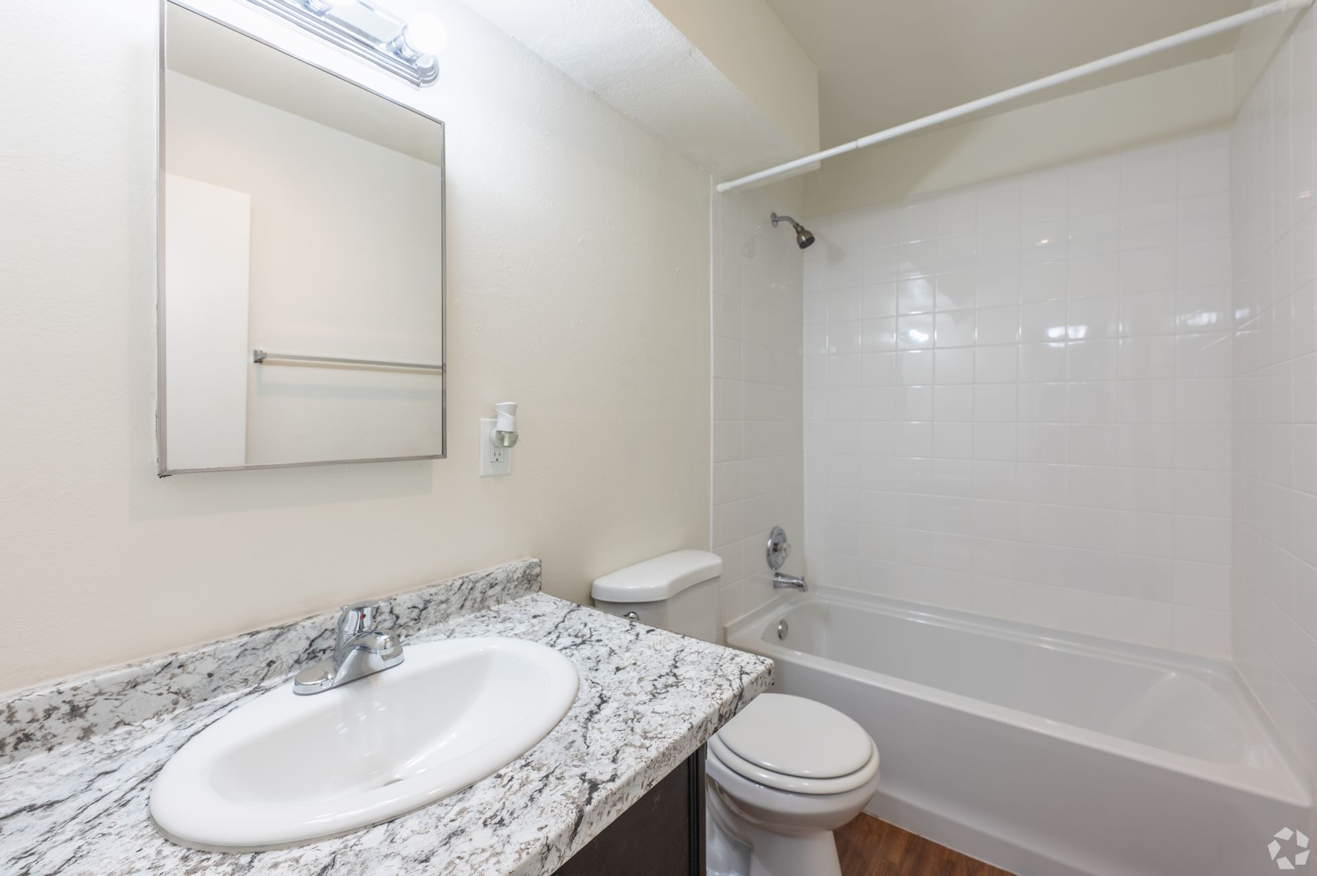 Bright bathroom with granite vanity, mirror, toilet, and white tub shower.
