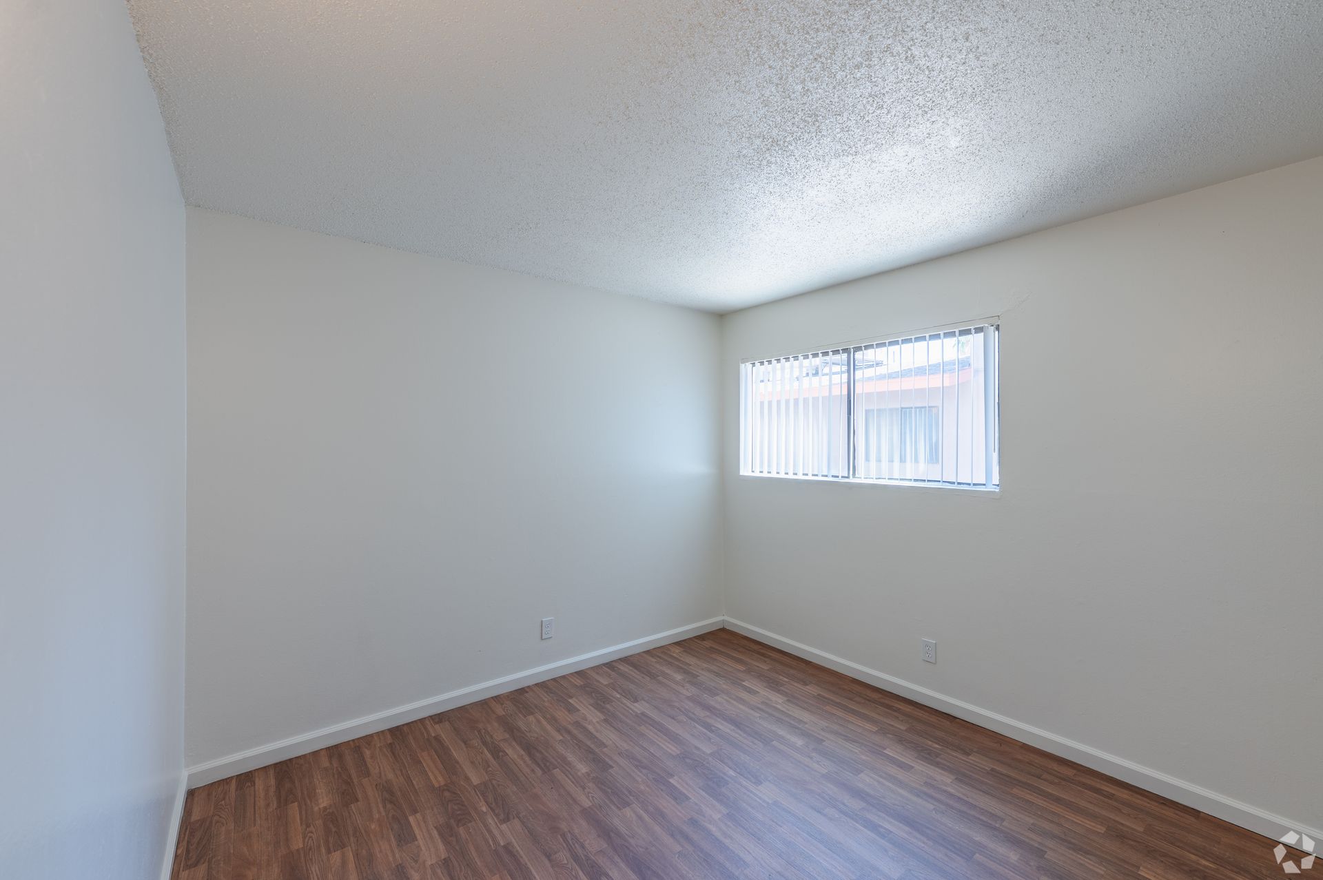 Empty beige room with wood-look flooring and a small window with blinds