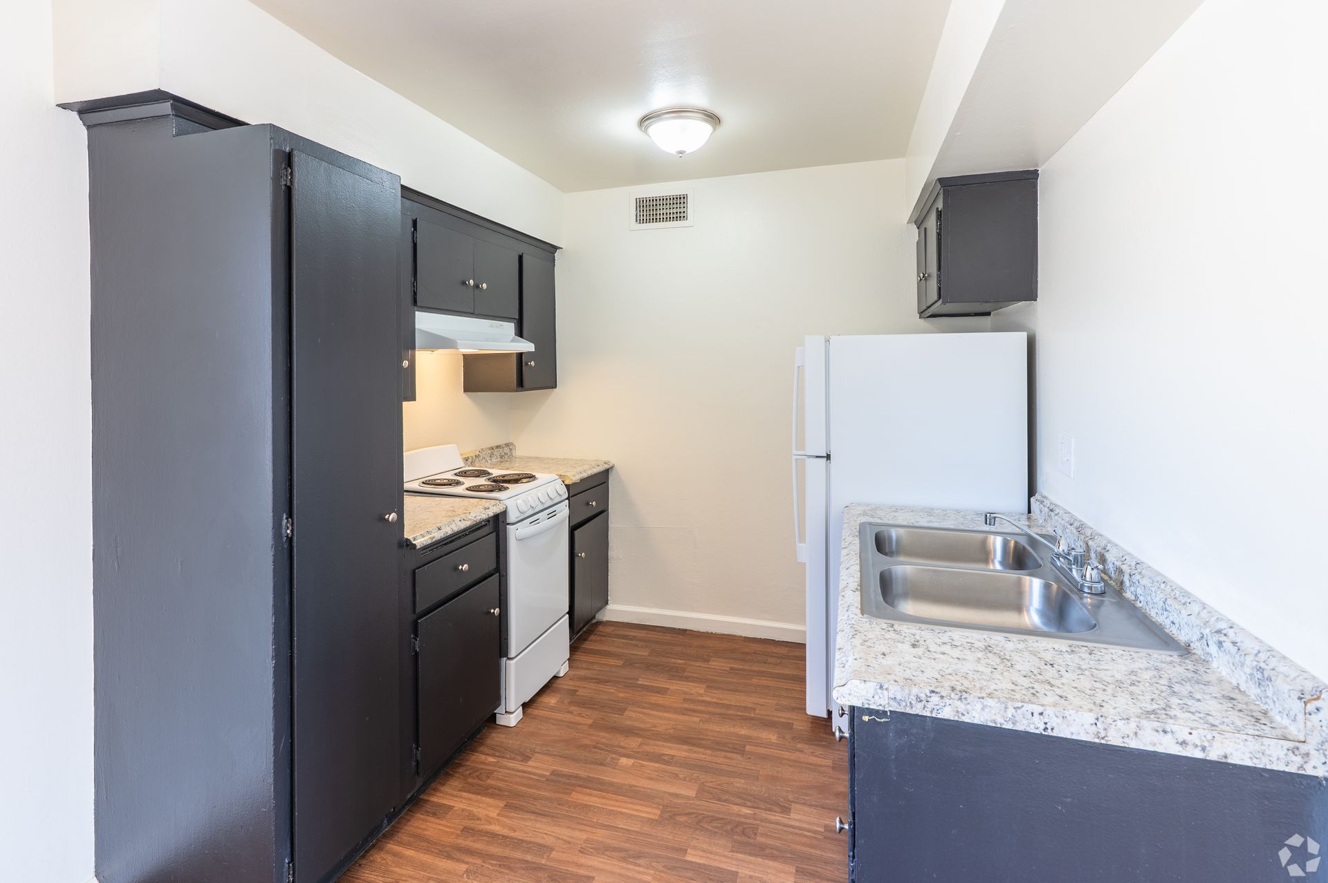 Small kitchen with dark cabinets, white appliances, granite counters, and wood floors