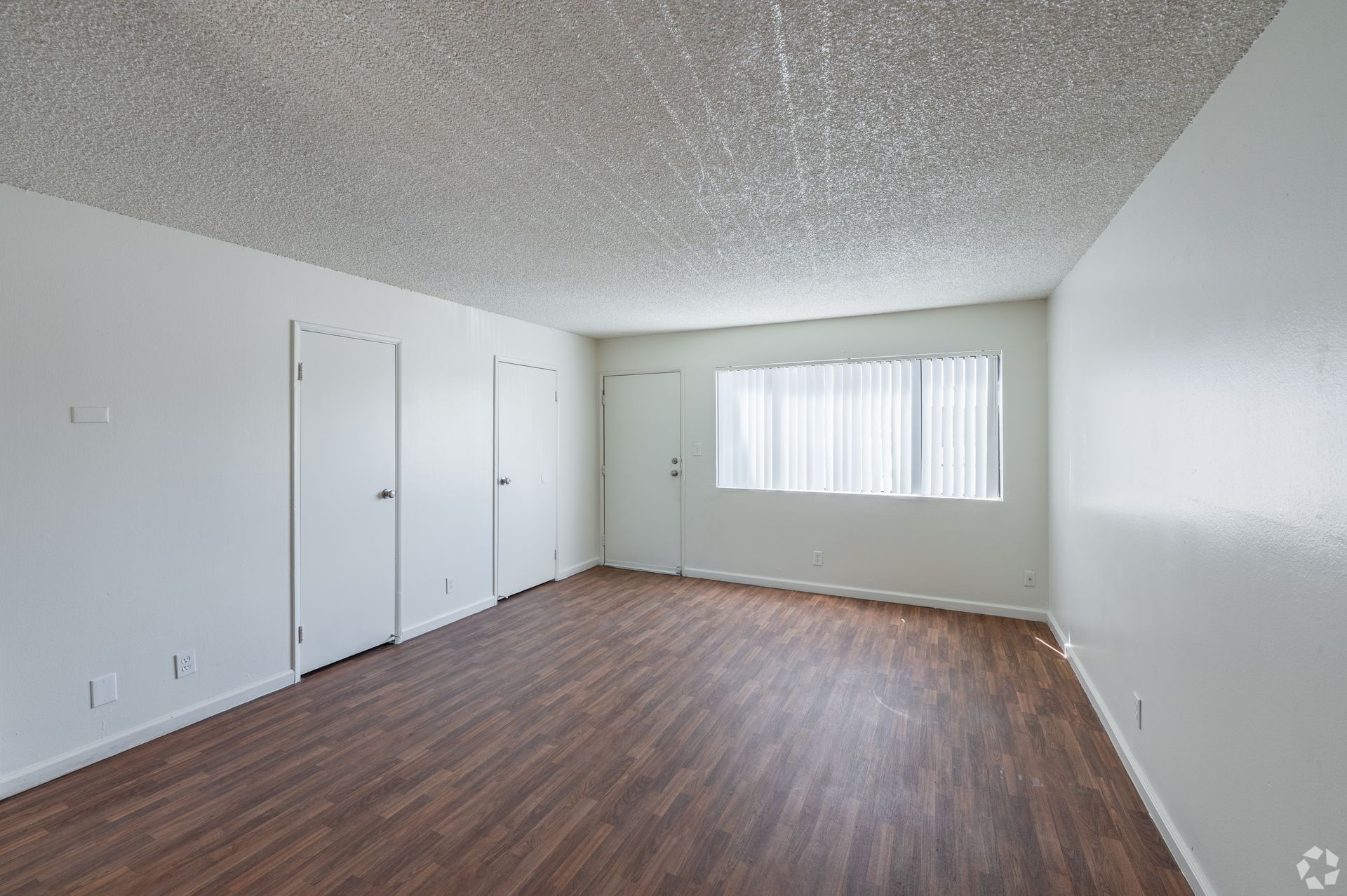 Empty room with wood-look floor, white walls, closet doors, and a window with blinds.