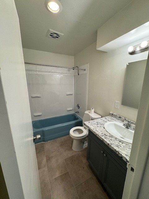 Small bathroom with shower tub, toilet, and dark vanity with granite countertop