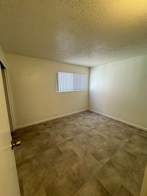 Empty beige room with patterned tile floor and a small window with vertical blinds.