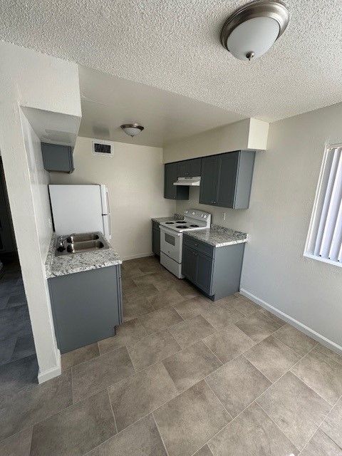 Small kitchen with gray cabinets, white stove, tiled floor, and vertical blinds by a bright window