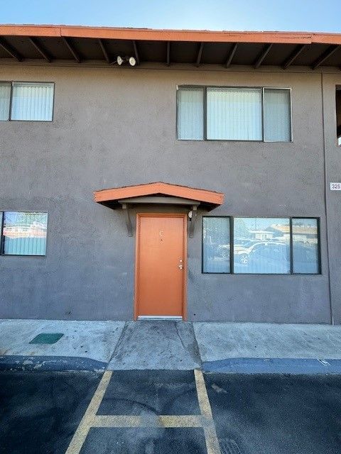 Apartment exterior with orange door, gray stucco walls, and parking spaces in front
