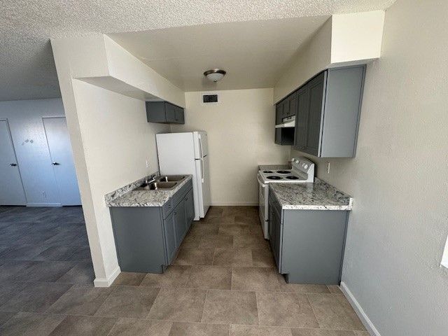 Small galley kitchen with gray cabinets, white appliances, and speckled countertops