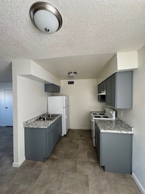 Small galley kitchen with gray cabinets, speckled counters, white appliances, and tiled floor.