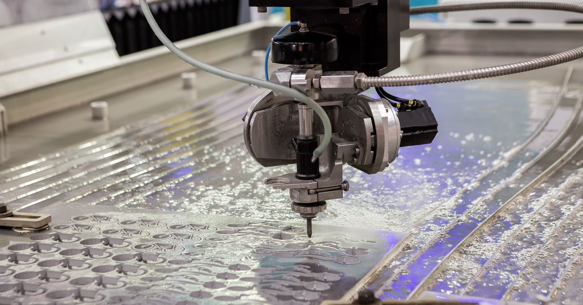 A CNC waterjet cutting machine with a large nozzle cutting small and precise shapes into a metal sheet.
