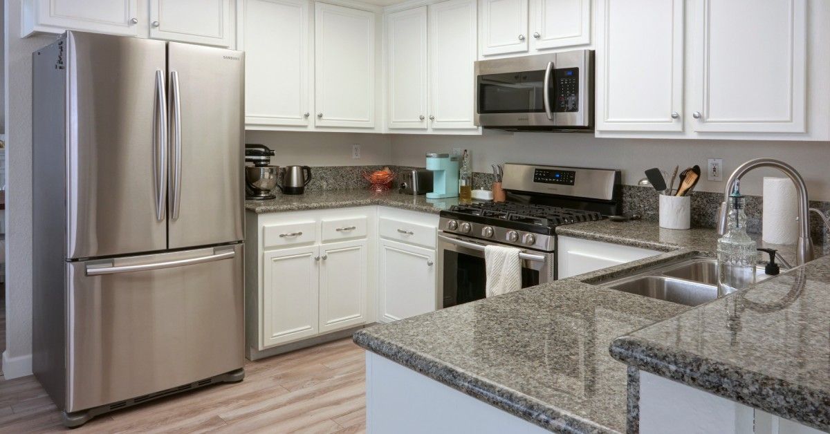 A contemporary kitchen with granite counters and white cabinets. The refrigerator, microwave, and range are stainless steel.