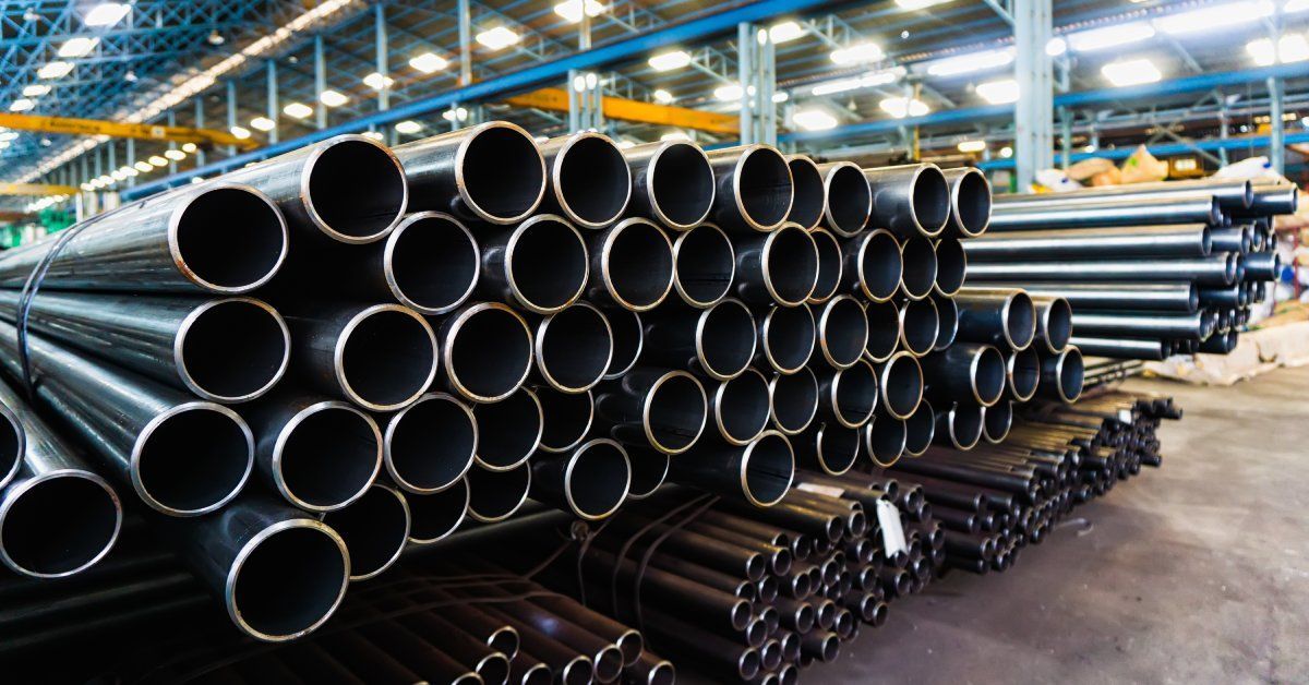 Large quantities of steel pipes are packed together in bundles inside a factory with high ceilings.