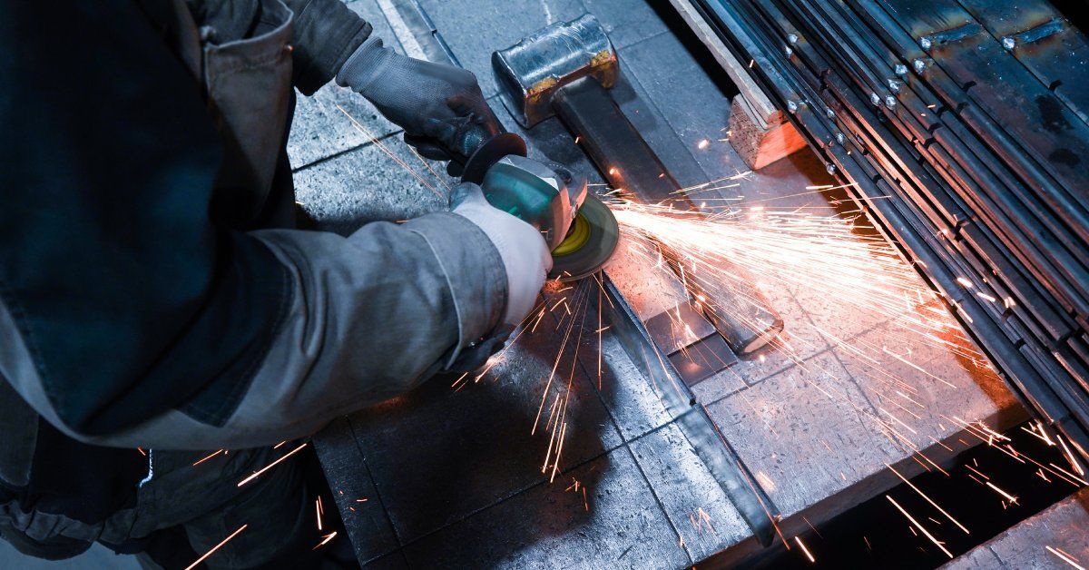 Orange sparks flying as a worker wearing thick gloves and an apron uses a tool to cut through stainless steel.