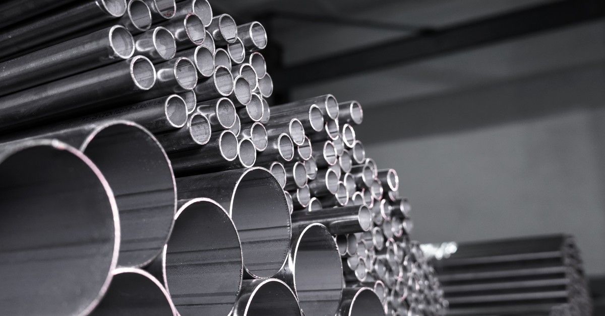 Steel pipes of various diameters and lengths are stacked in organized rows inside a warehouse facility.