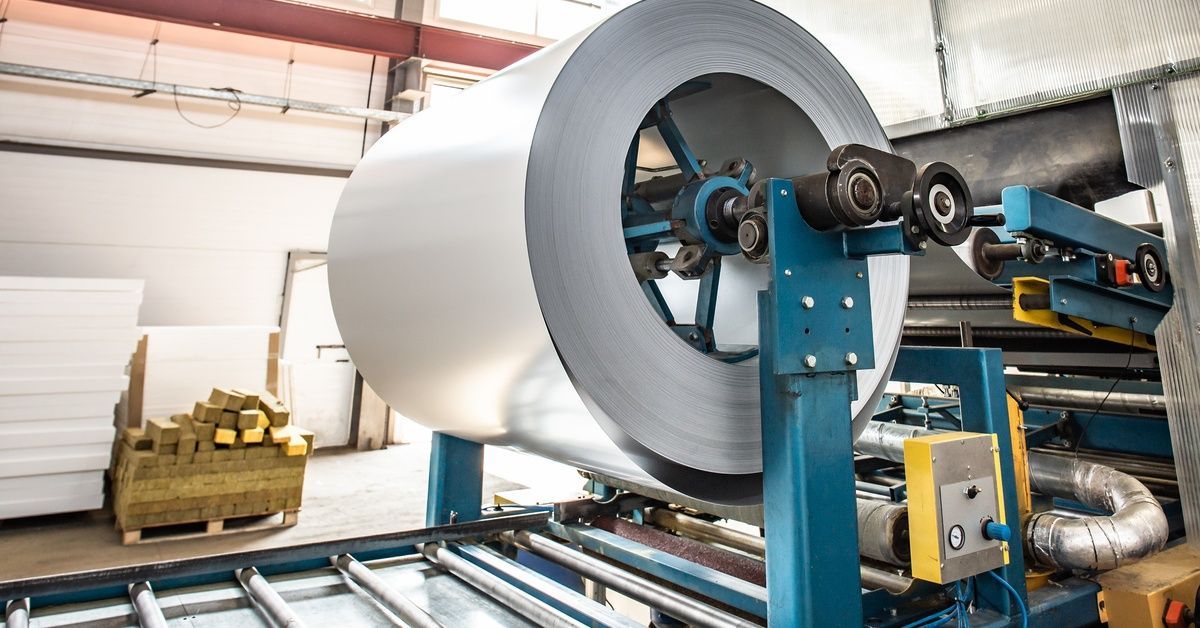 Stainless steel coil mounted on industrial machinery in a manufacturing facility, with rollers and p