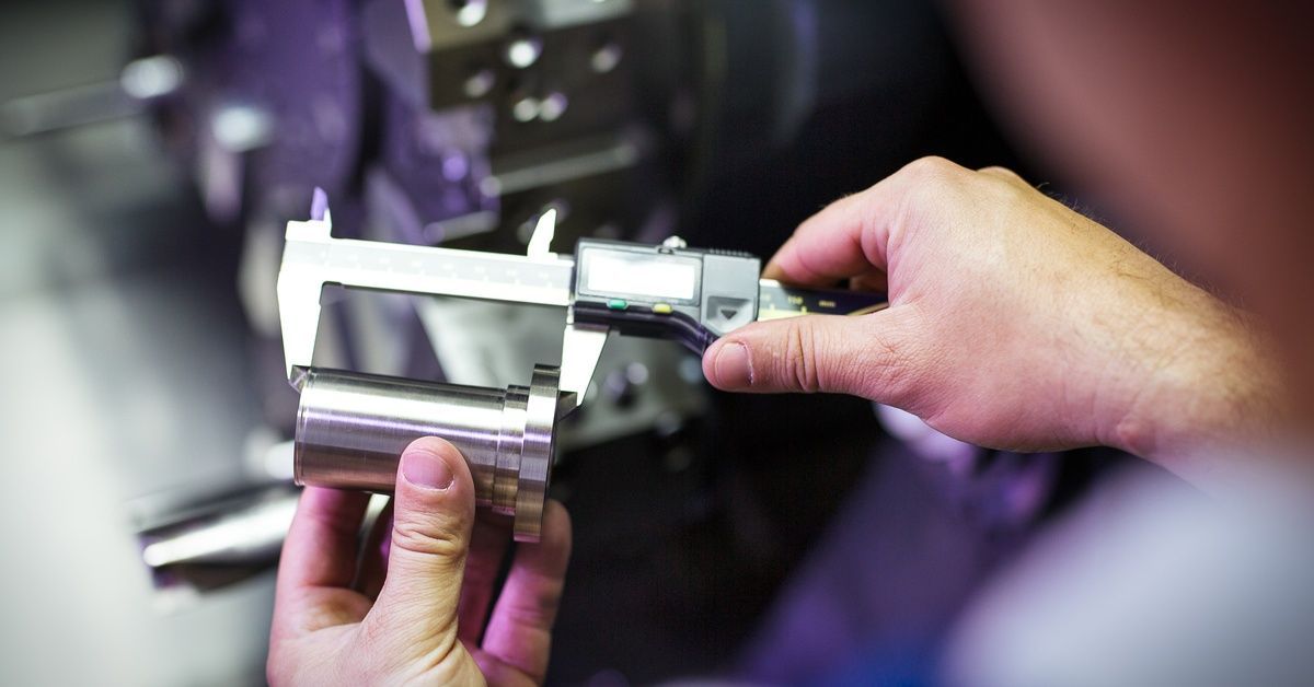 A technician uses digital calipers to measure a machined metal component in a precision fabrication 